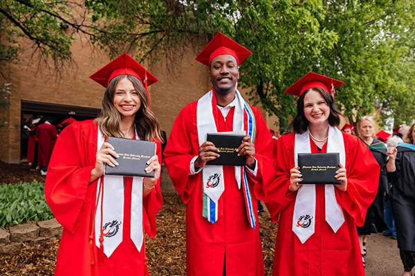 Three students in red cap and gown holding diploma sleeve