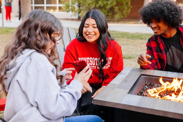 Three students sitting at fire table