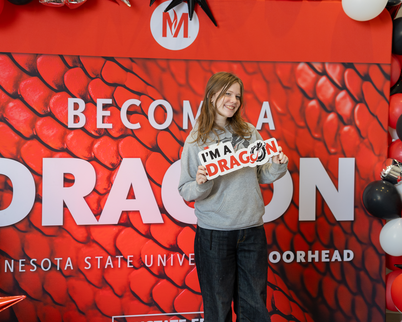 Smiling student holds a sign that reads 'I'm a Dragon'
