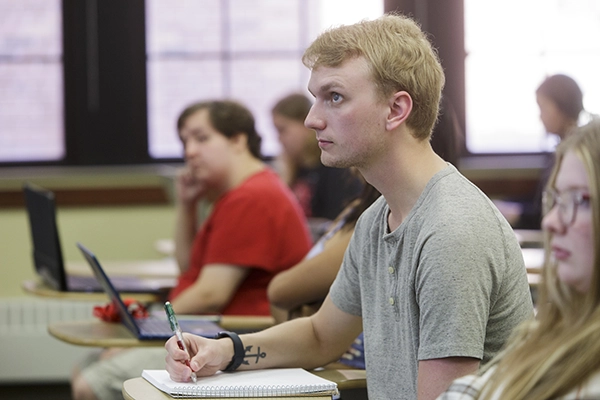 Student sitting in classroom with other students taking notes